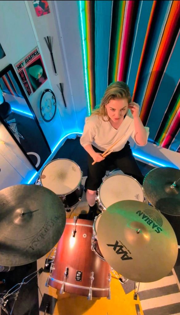 Vrouwelijke leerling achter het drumstel tijdens een drumles in de sfeervol verlichte studio van Drumschool Utrecht